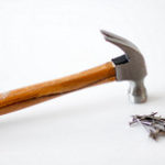 Image of a hammer with a wooden handled resting face down on a white surface with a small pile of 2" nails nearby