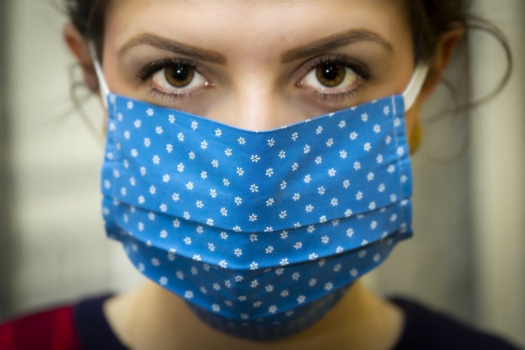 Brown eyed woman facing camera wearing a navy blue with white spotted mask