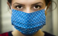 Brown eyed woman facing camera wearing a navy blue with white spotted mask