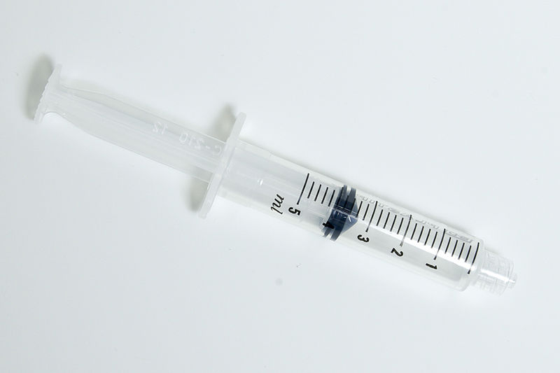 Photo looking down on a fat plastic syringe with a blunt end (no needle) with the plunger pulled partially back against a neutral light surface.