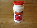 Stock photo of a regular sized Tylenol bottle with a red label and cap sitting on a wooden surface.
